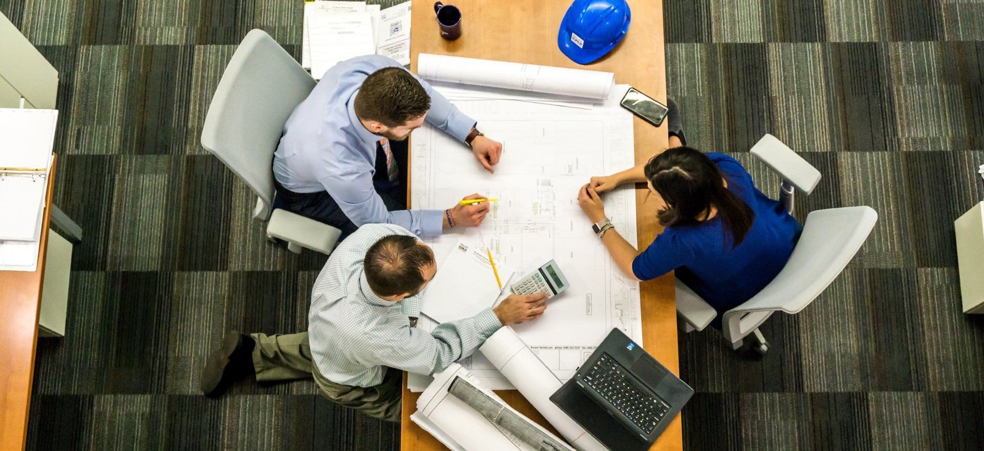 A group of people are sitting around a table looking at a blueprint.