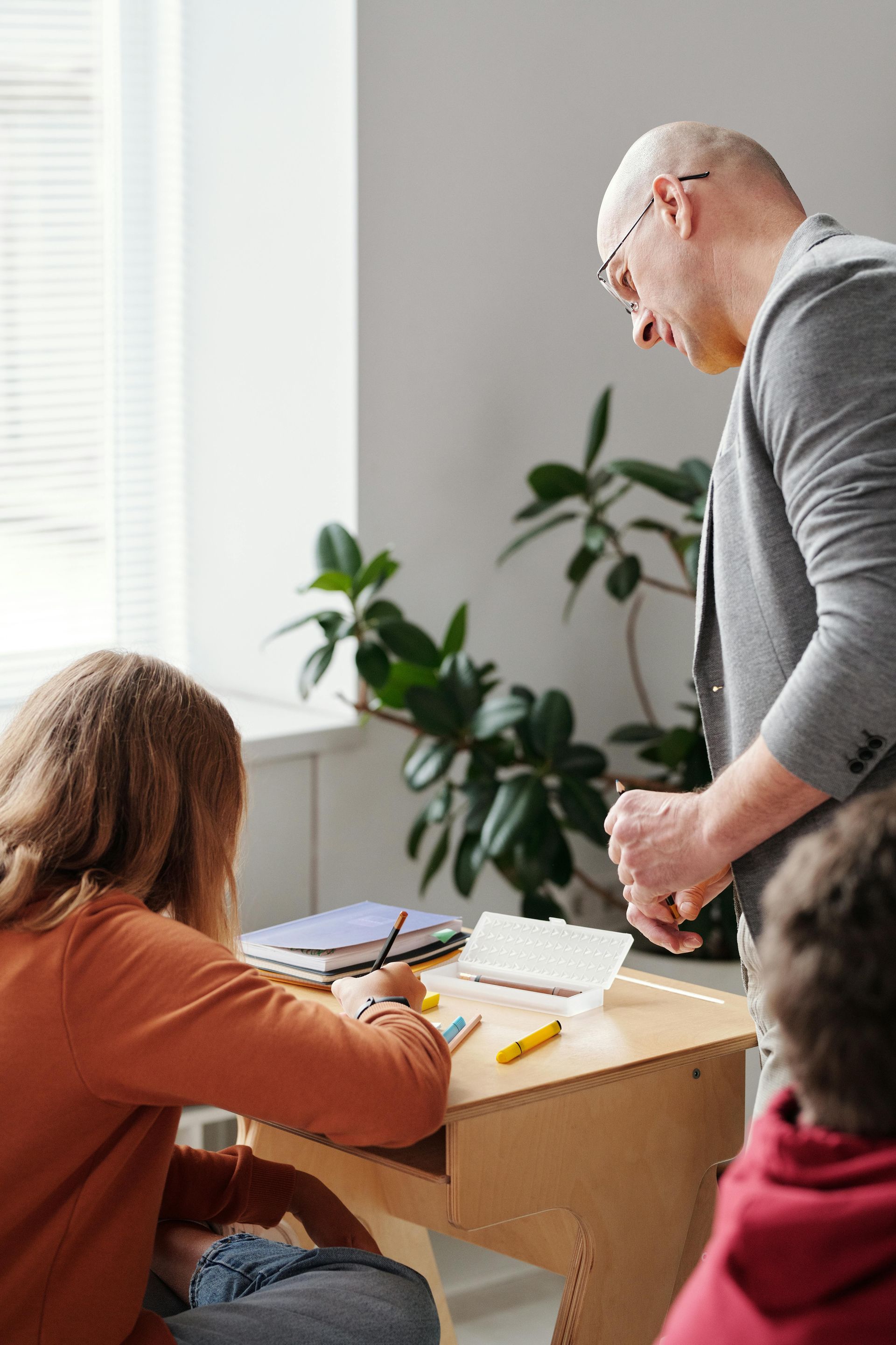 A man is standing next to a group of children sitting at a desk.