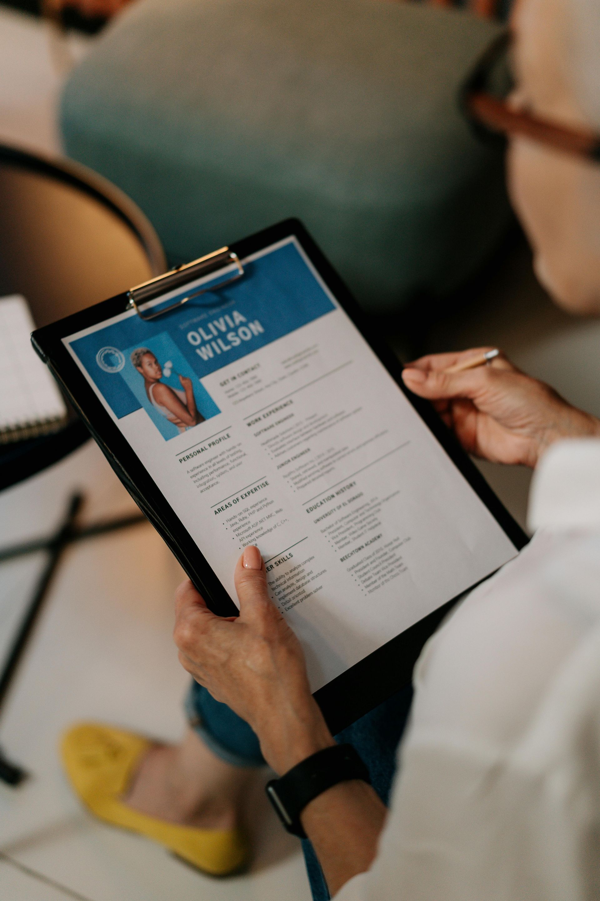 A woman is holding a clipboard with a resume on it.
