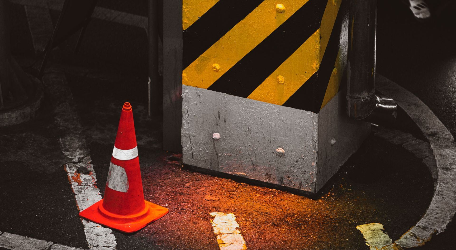 A red and white traffic cone is sitting next to a yellow and black striped block.