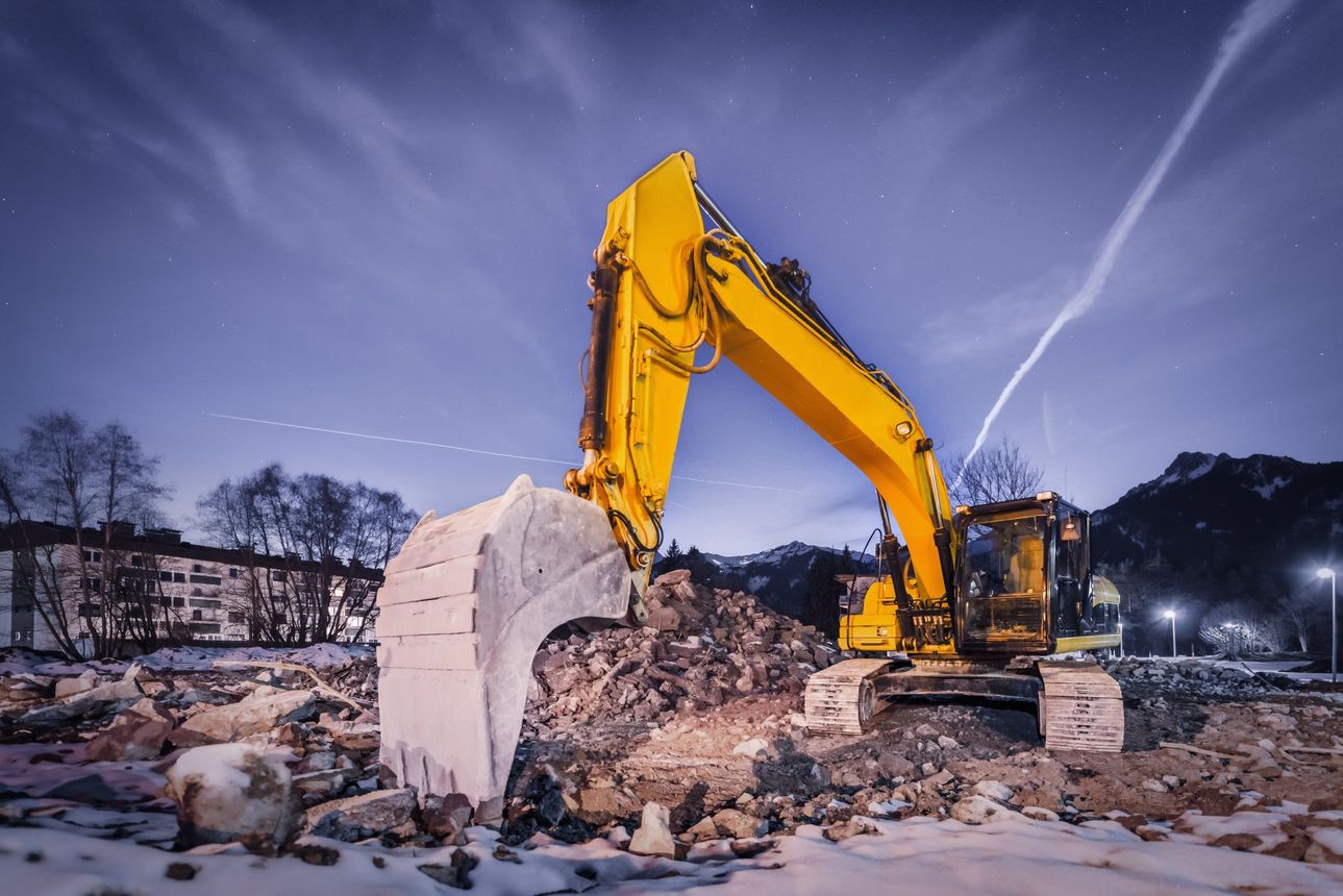 A yellow excavator is working on a construction site at night.