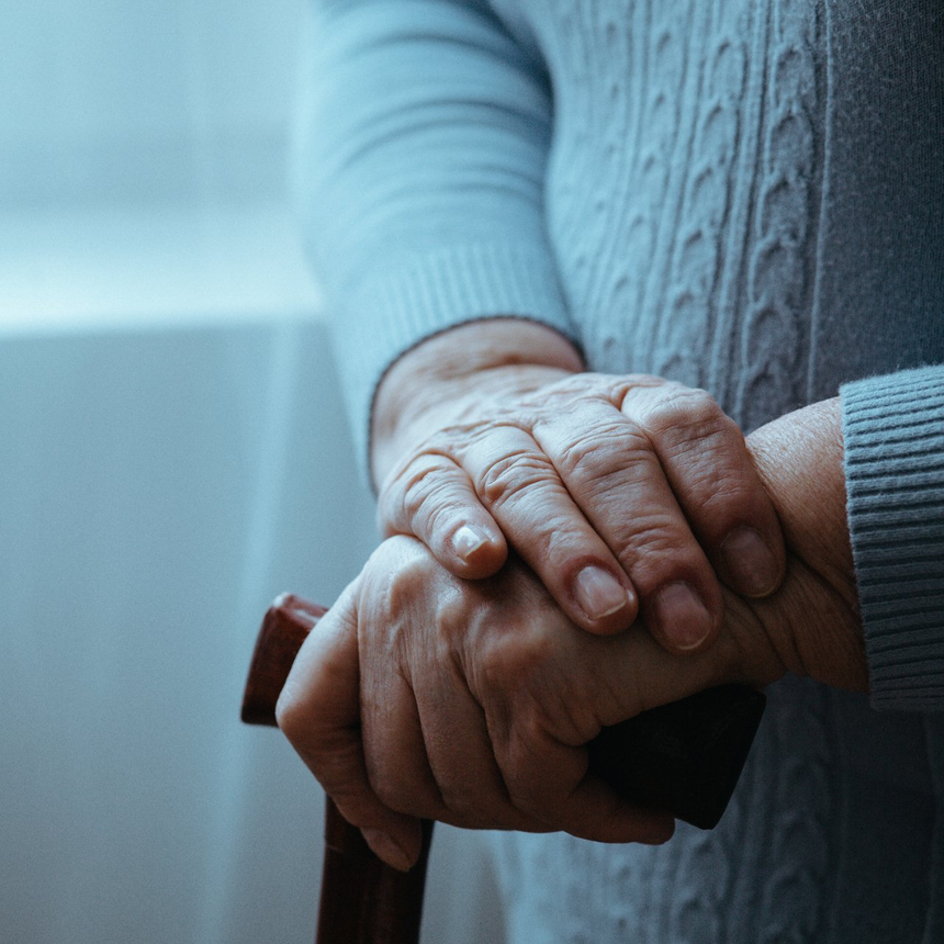 An elderly woman is holding a cane in her hands.