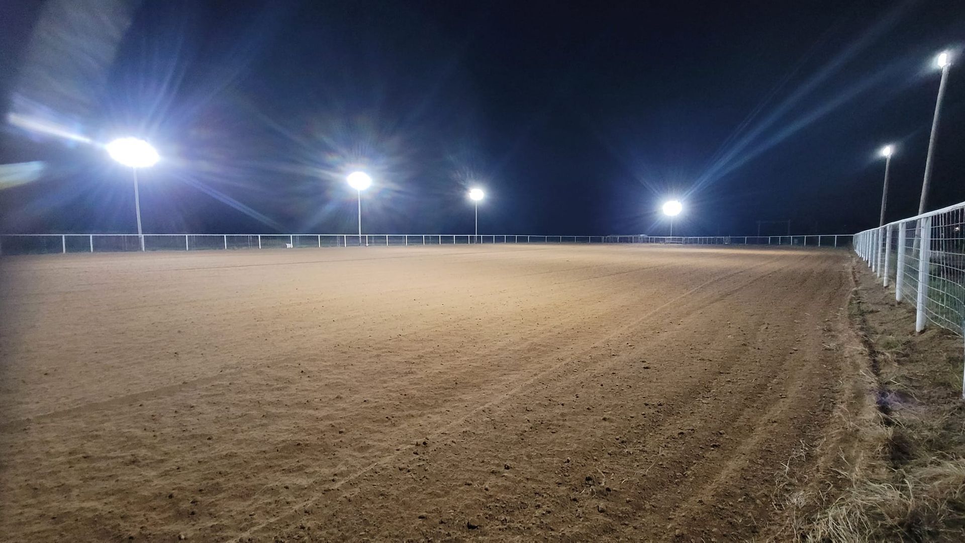 A dirt field arena with a fence and lights at night