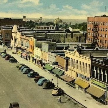 A row of cars are parked on the side of a downtown street