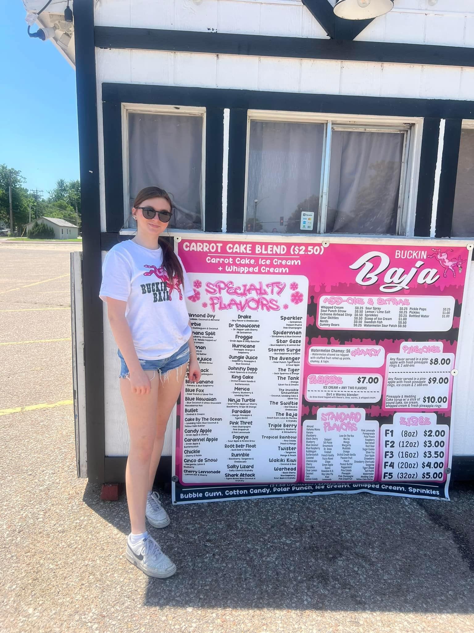A woman is standing in front of a menu in a parking lot.