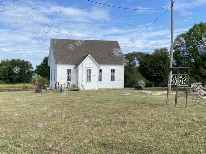 The Bland School House A white house is sitting in the middle of a grassy field surrounded by soap bubbles.