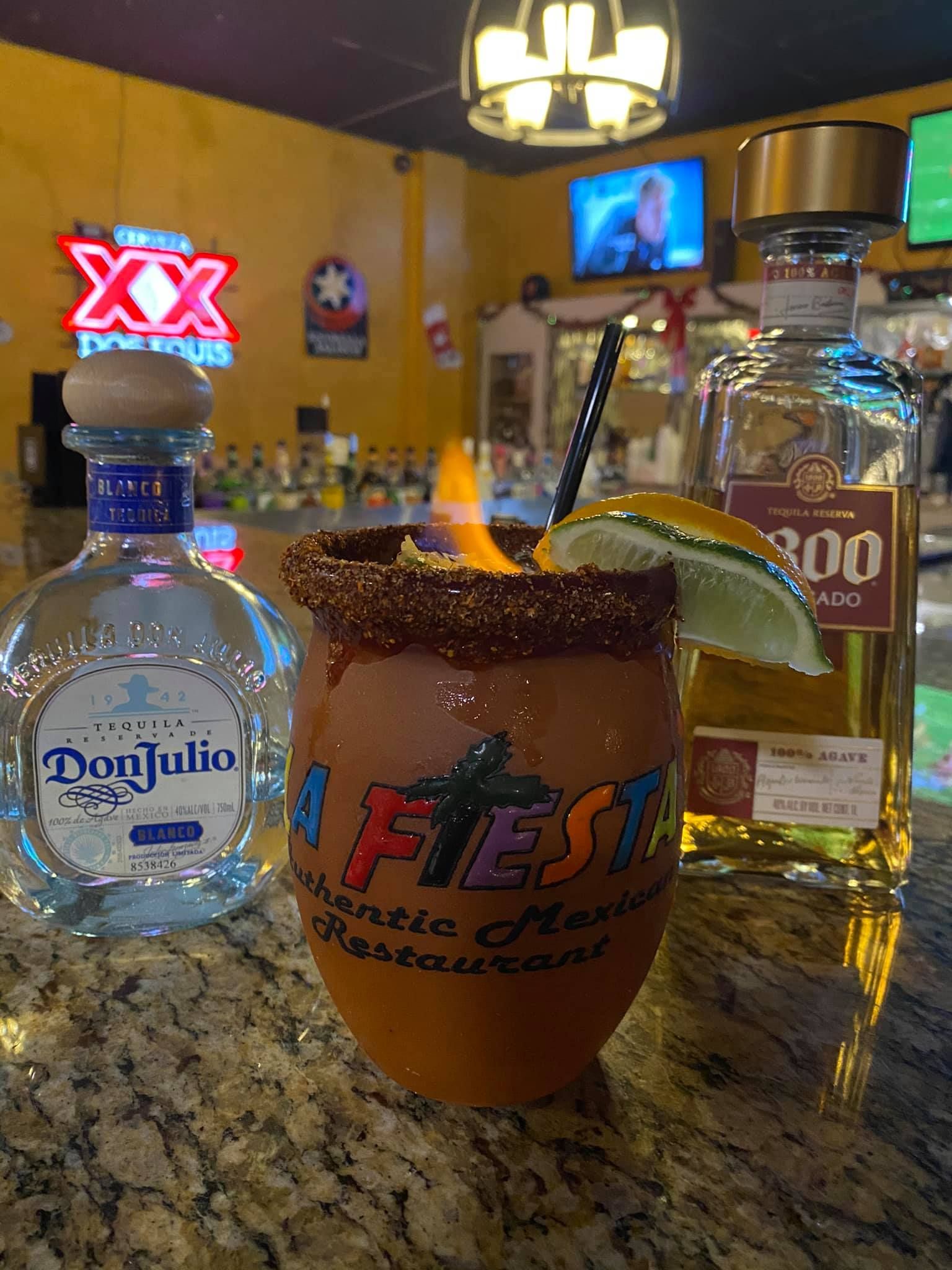 A margarita is sitting on a bar next to a bottle of tequila.