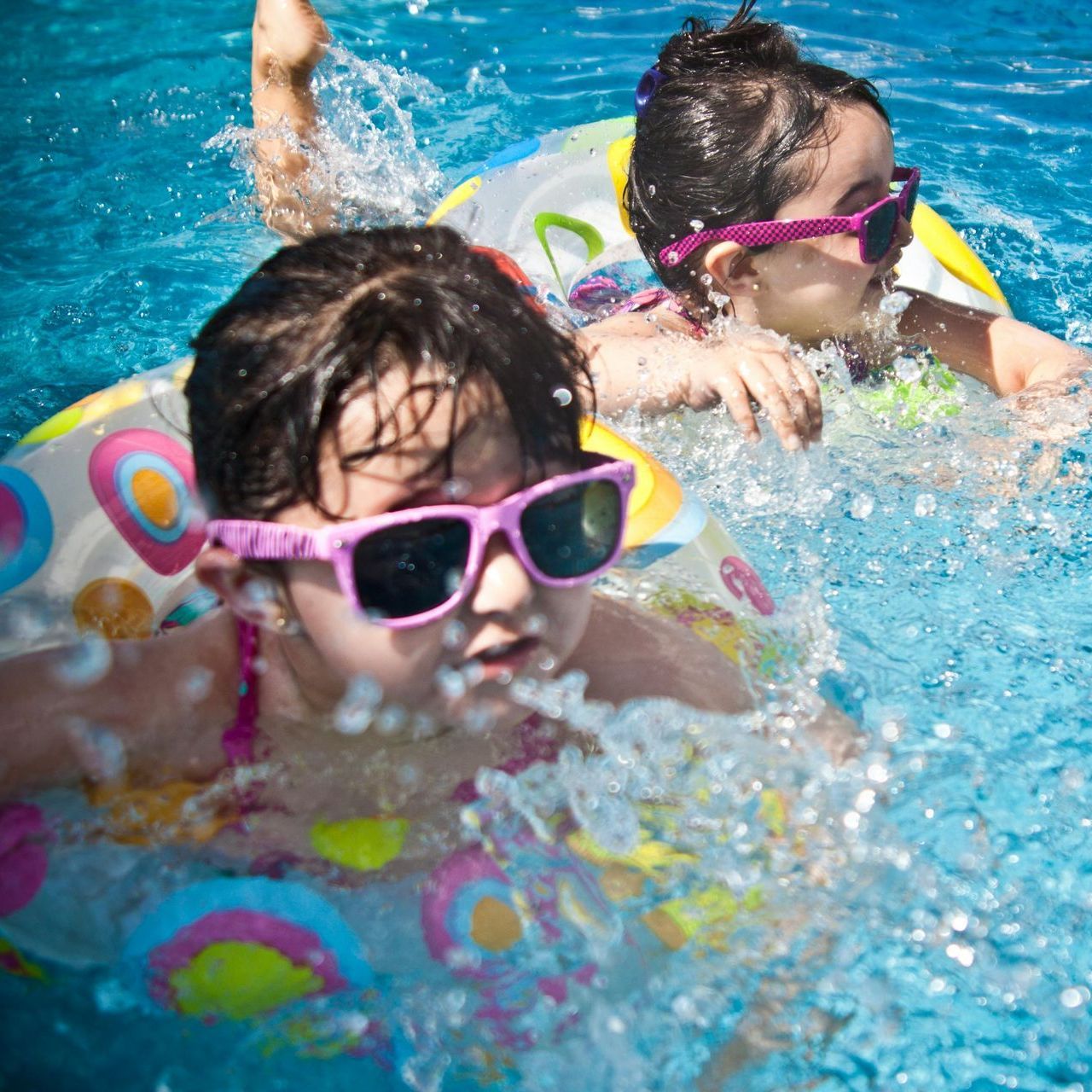 Two girls wearing sunglasses are swimming in a pool