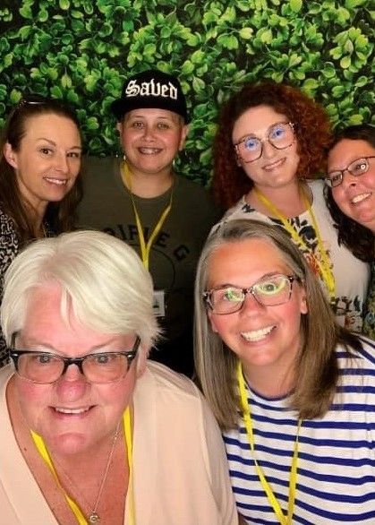 A group of women posing for a picture with one wearing a salute hat