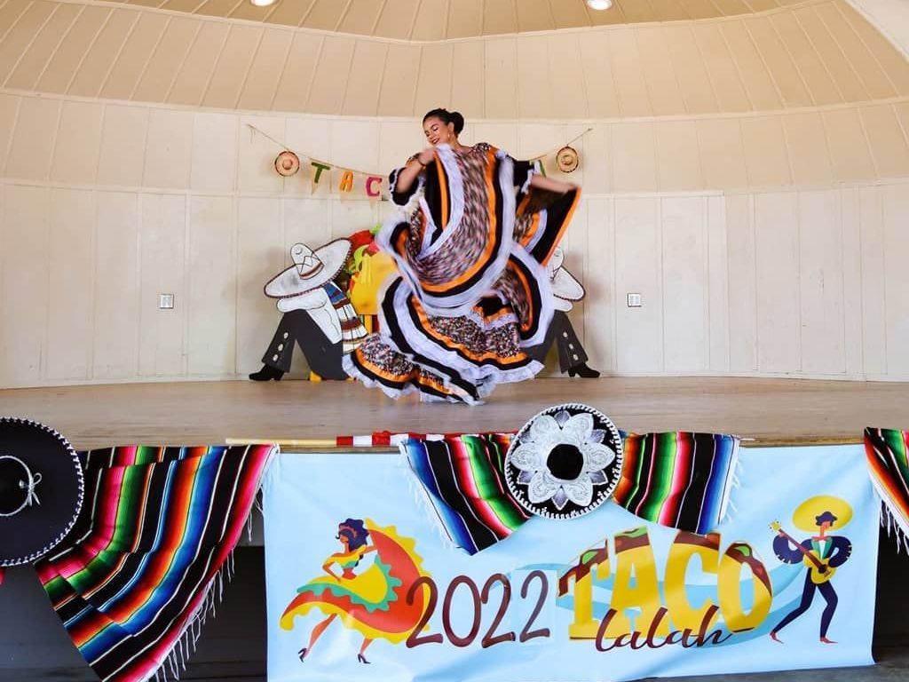 A woman is dancing on a stage in front of a sign that says 2022 tacos