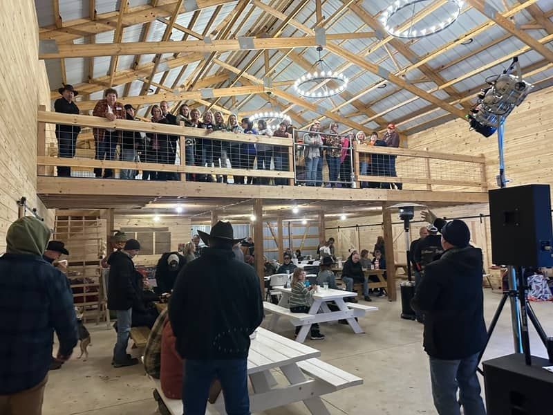 Triple G Ranch event venue A group of people are sitting at picnic tables in a barn.
