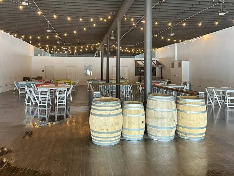 Venue 208 in Ark City, KS A large room with tables and chairs and wooden barrels on the floor.
