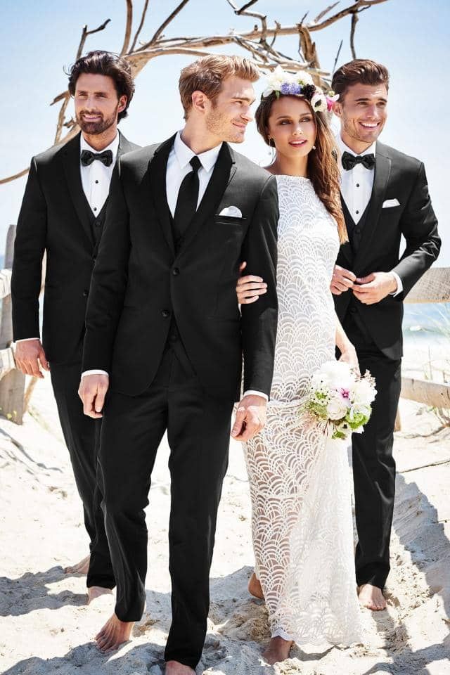 A bride and her groomsmen are walking barefoot on the beach.