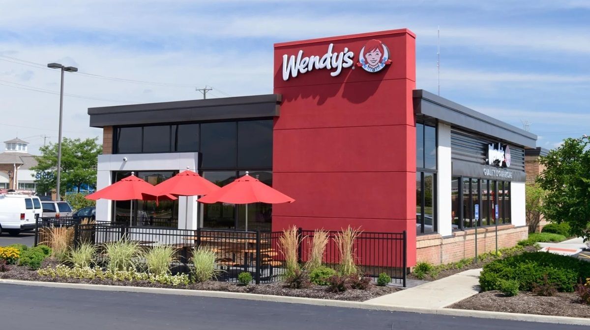 A wendy 's restaurant with red umbrellas in front of it.