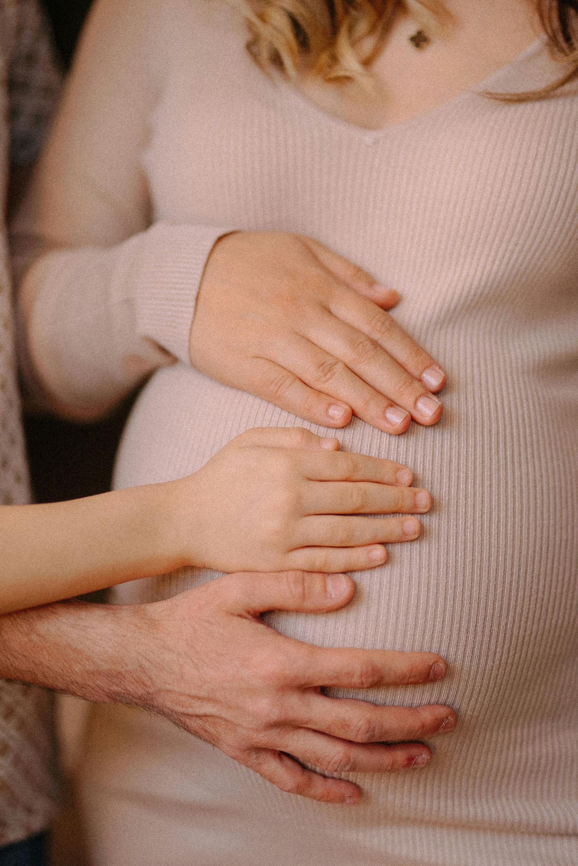 Pregnant person in a pink dress, hands on belly, another person's hand on belly.