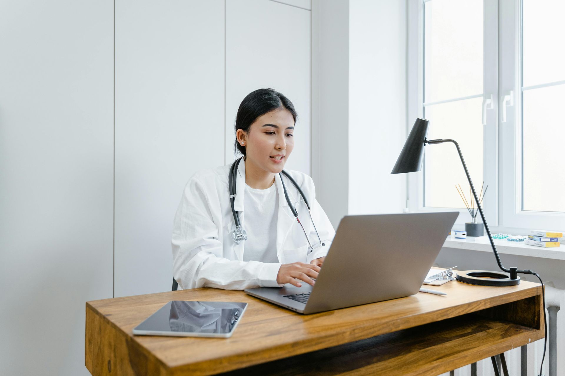 A doctors is talking and typing on a laptop computer