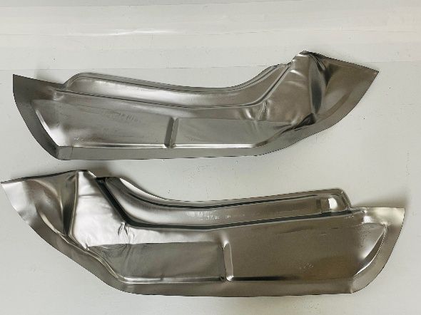 Two shiny, curved metal car floor pans, possibly replacements, against a white background.