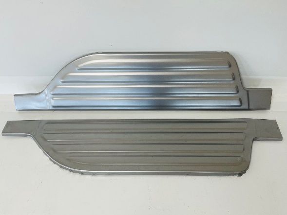 Two metal running board replacements with horizontal grooves, lying on a white surface.