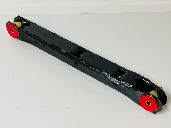 Black car suspension arm with red and yellow bushings, lying on a white surface.
