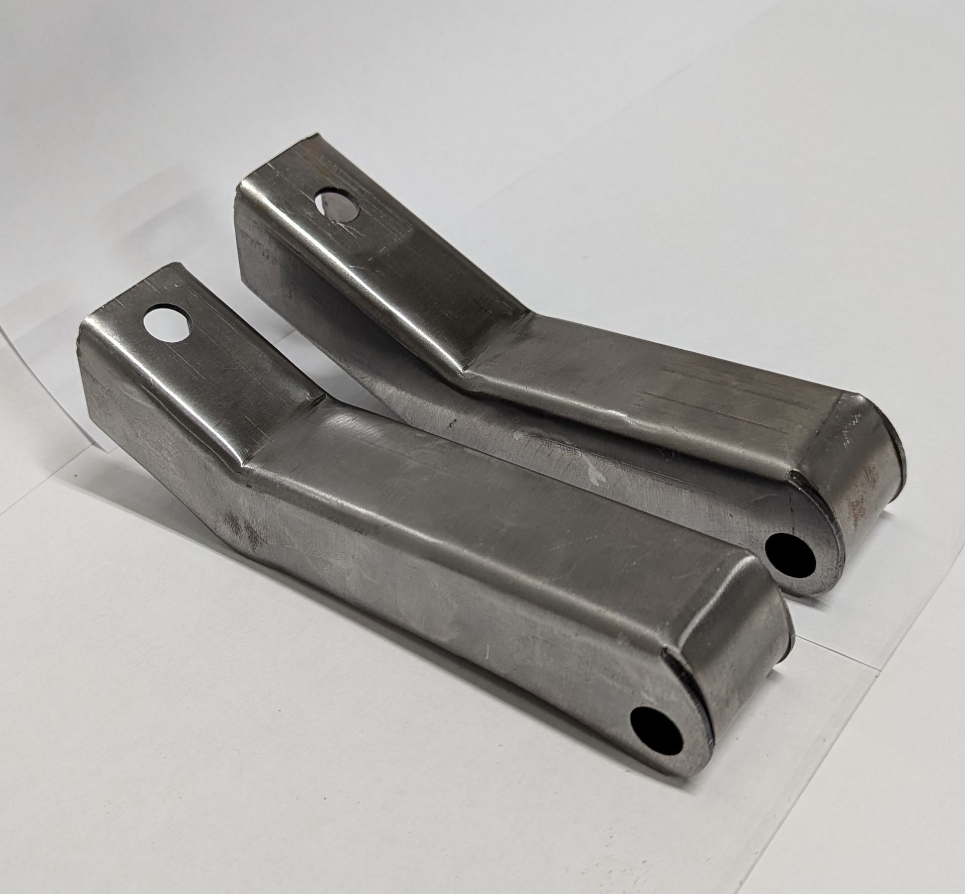 Two pieces of metal with holes in them are sitting on a white surface.