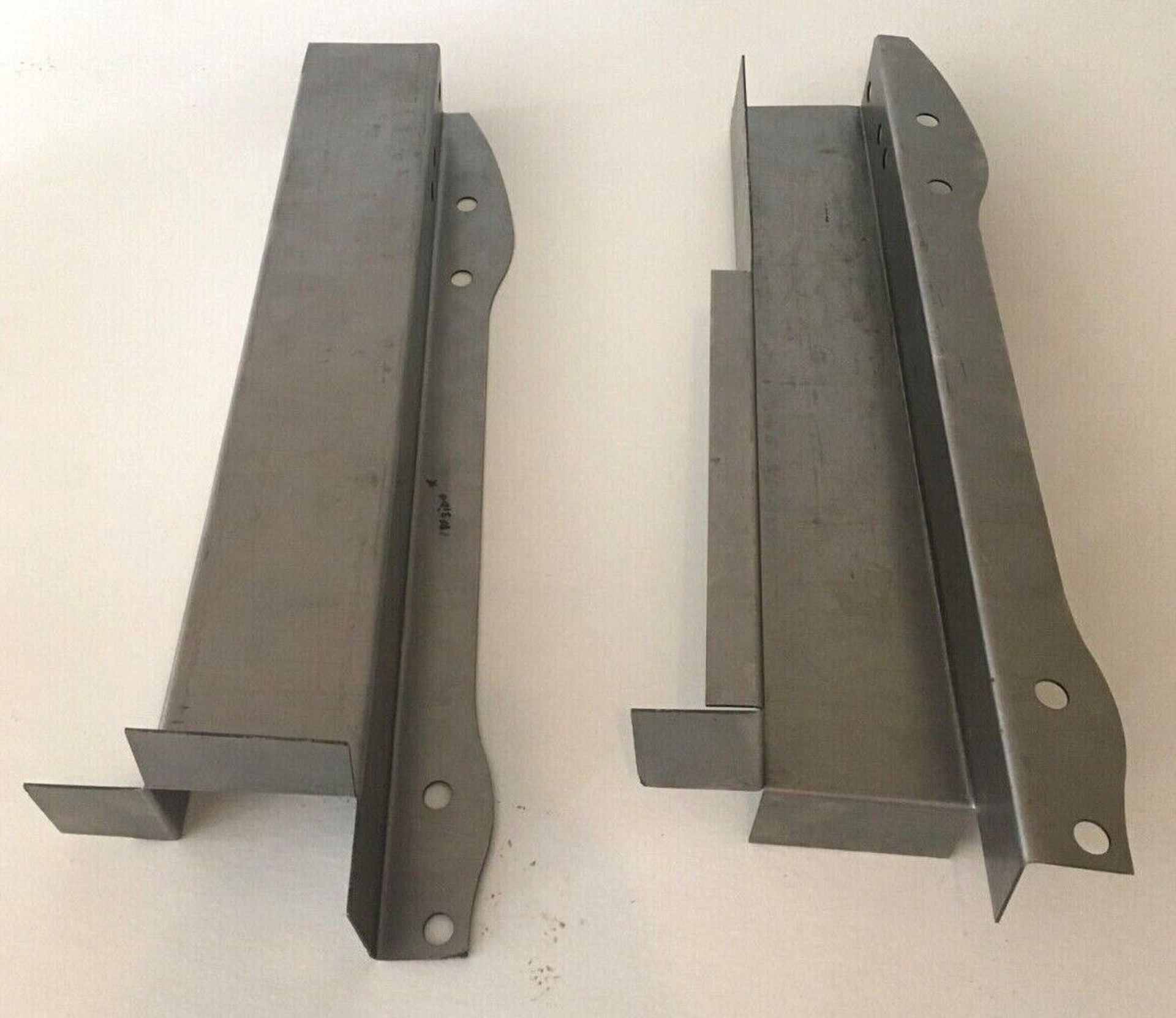 A pair of metal brackets with holes in them on a white surface