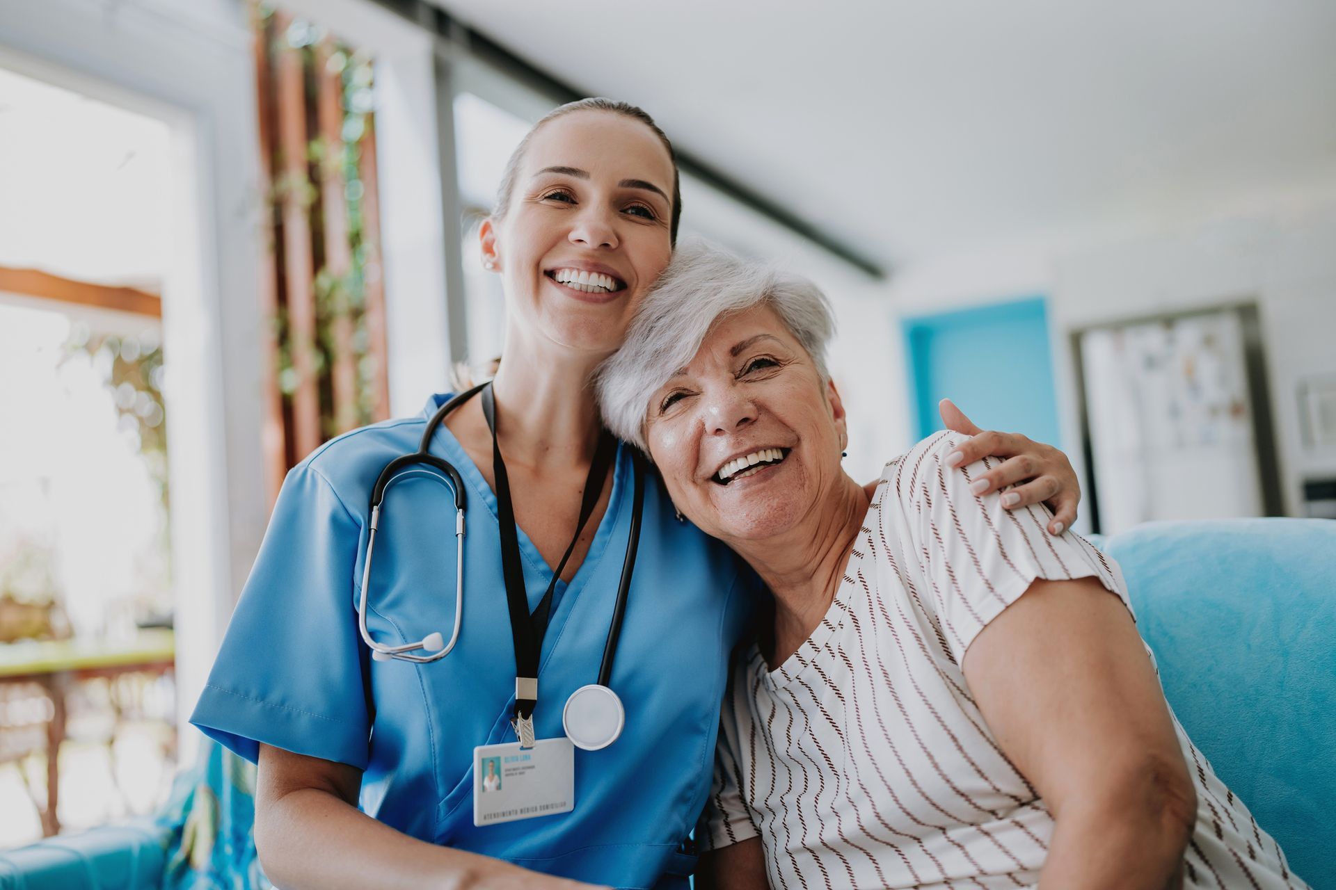 A nurse is sitting next to an elderly woman on a couch.