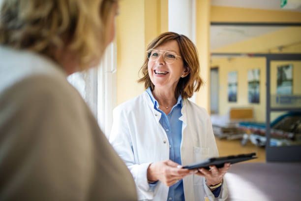A doctor is talking to a patient in a hospital while holding a clipboard.