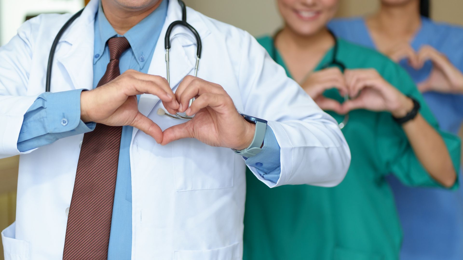A doctor and two nurses are making a heart shape with their hands.