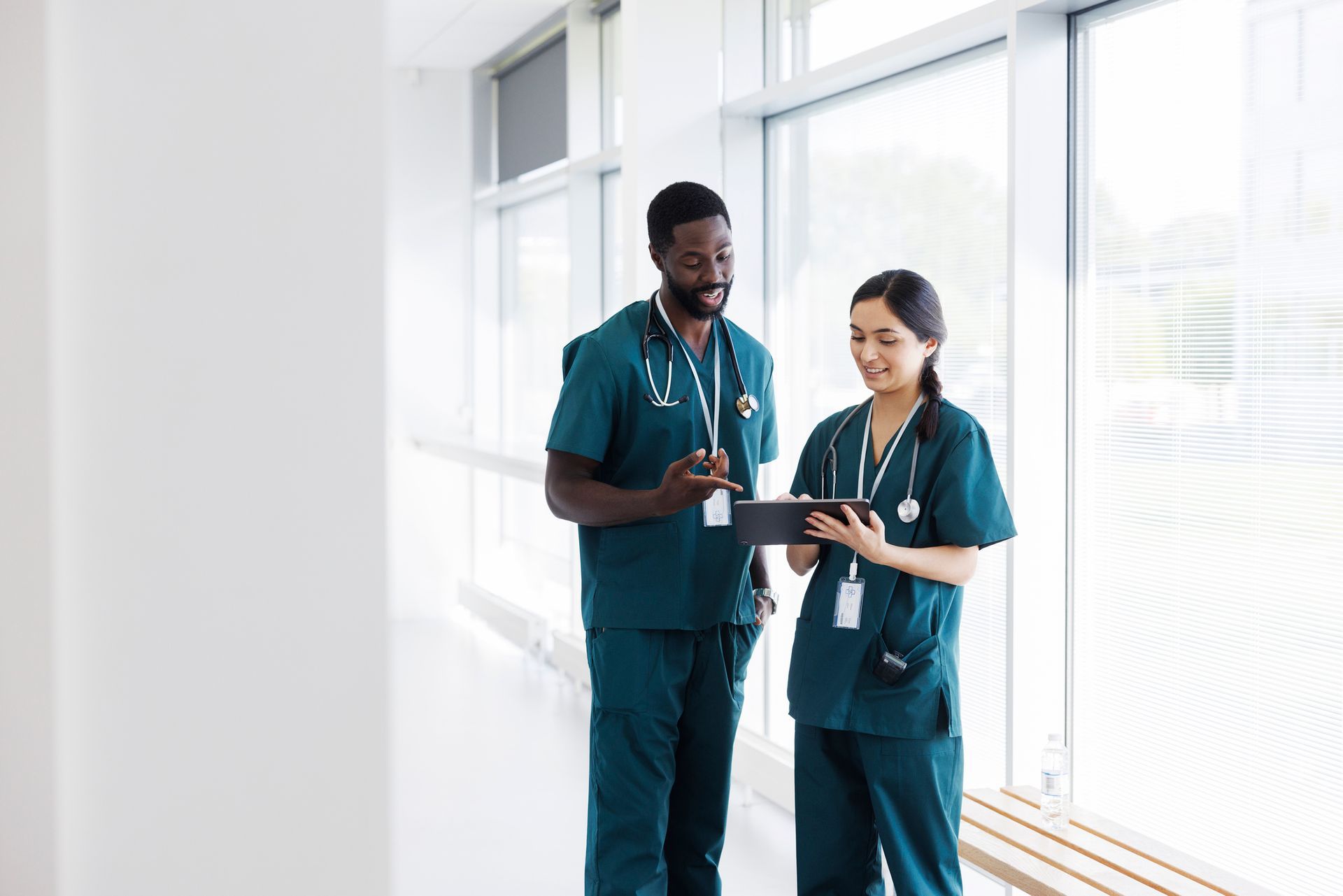 A man and a woman are standing in a hallway looking at a tablet.