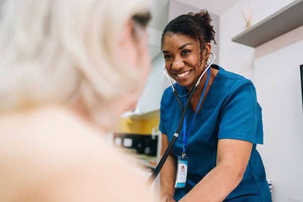 A nurse is smiling while listening to a patient 's heartbeat with a stethoscope.