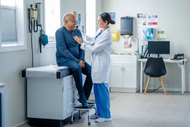 A doctor is listening to a old man patient 's heartbeat with a stethoscope.