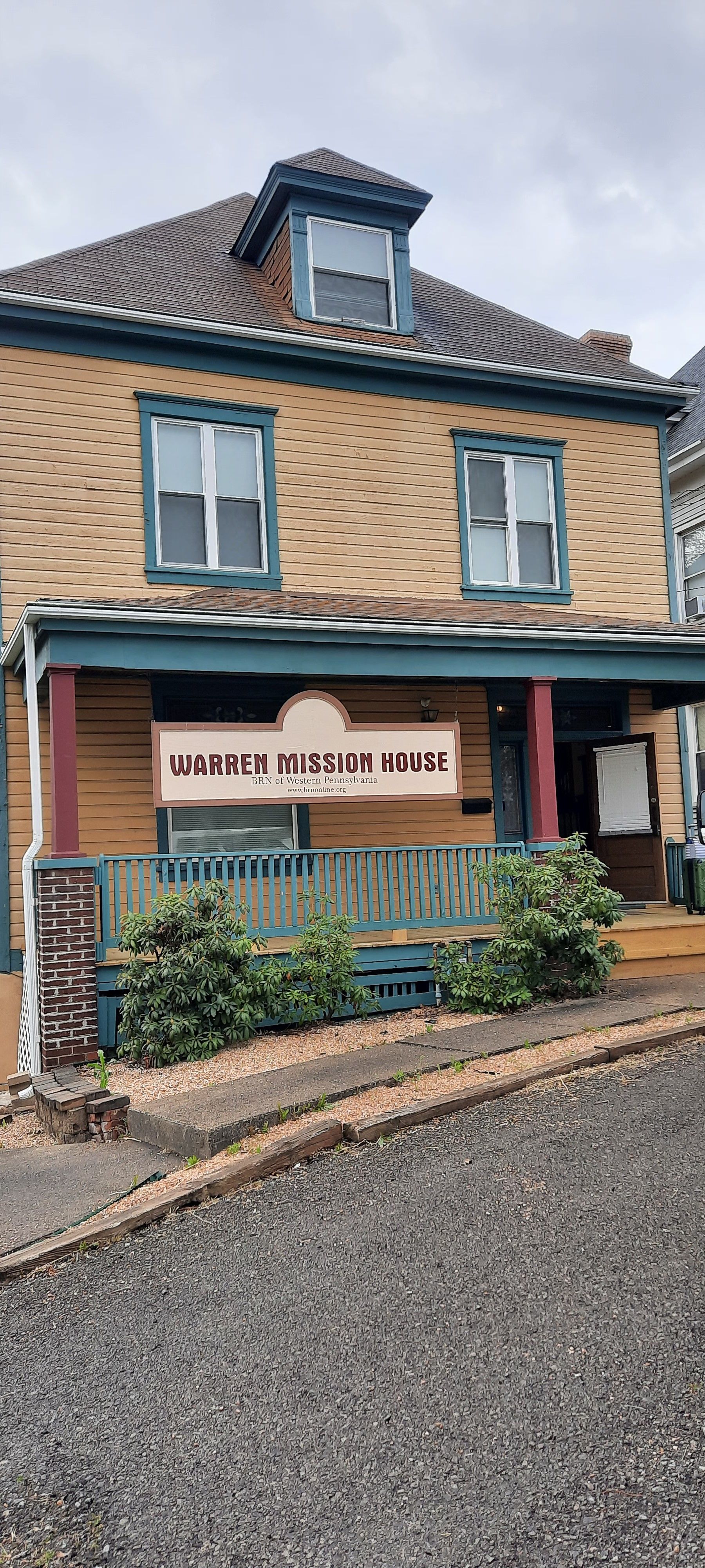 A large brick house with a porch and a sign on it.