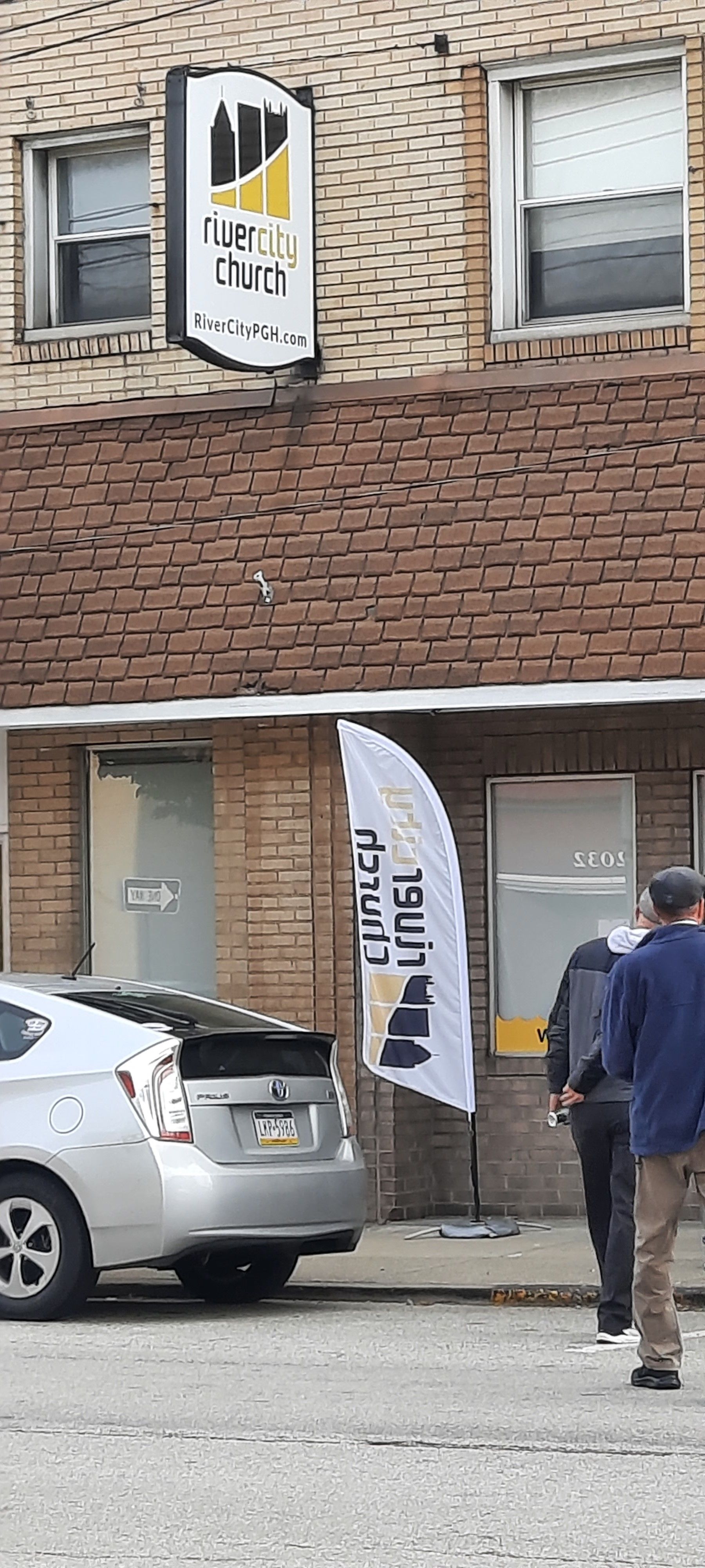 A group of people are standing in front of a building with a car parked in front of it.