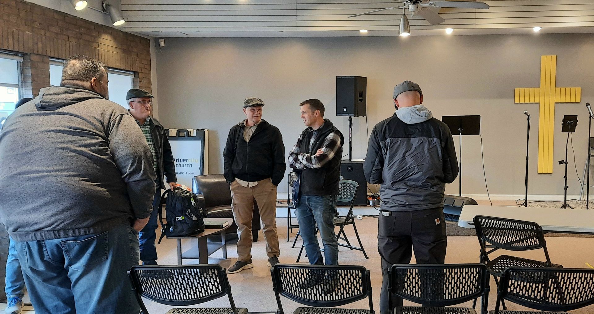 A group of men are standing in a room with a cross on the wall.