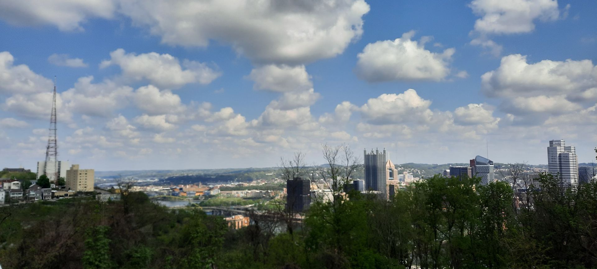 A city skyline with trees in the foreground and clouds in the background.