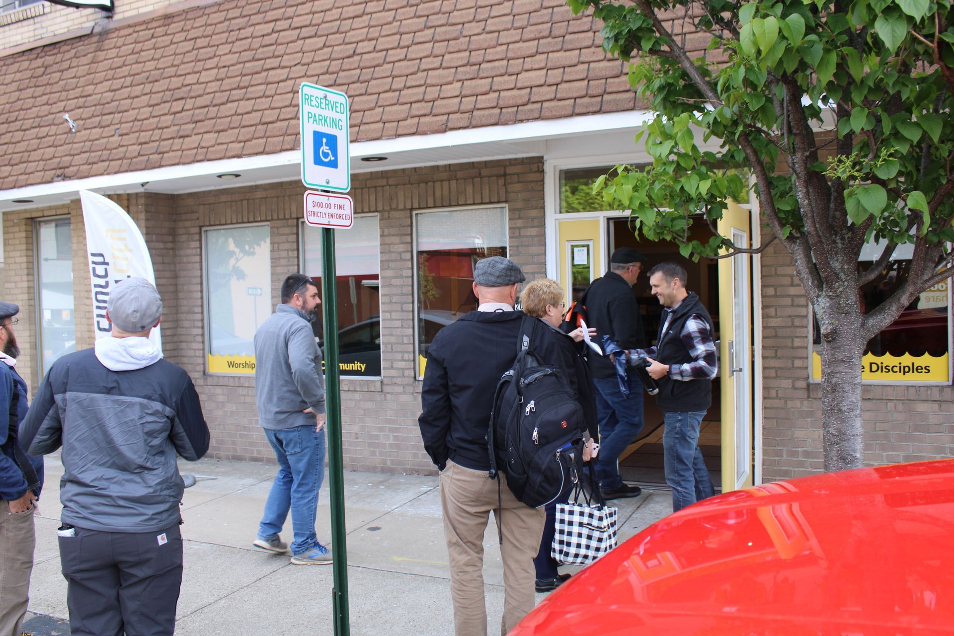 A group of people standing outside of a building with a handicapped parking sign