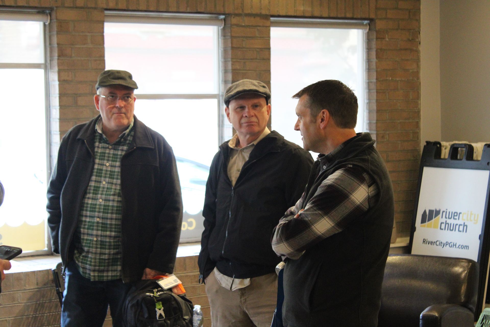 Three men are standing next to each other in a room with a sign that says ' a few cents ' on it