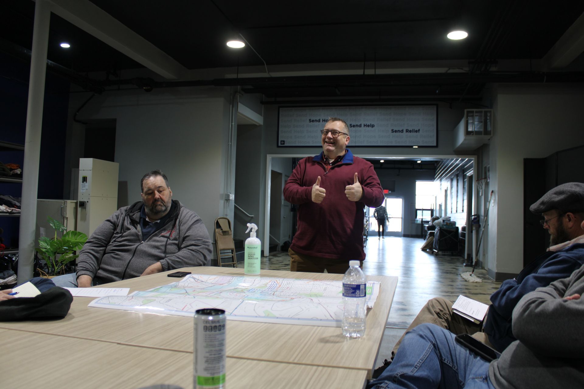 A man is giving a thumbs up while sitting at a table with other men.
