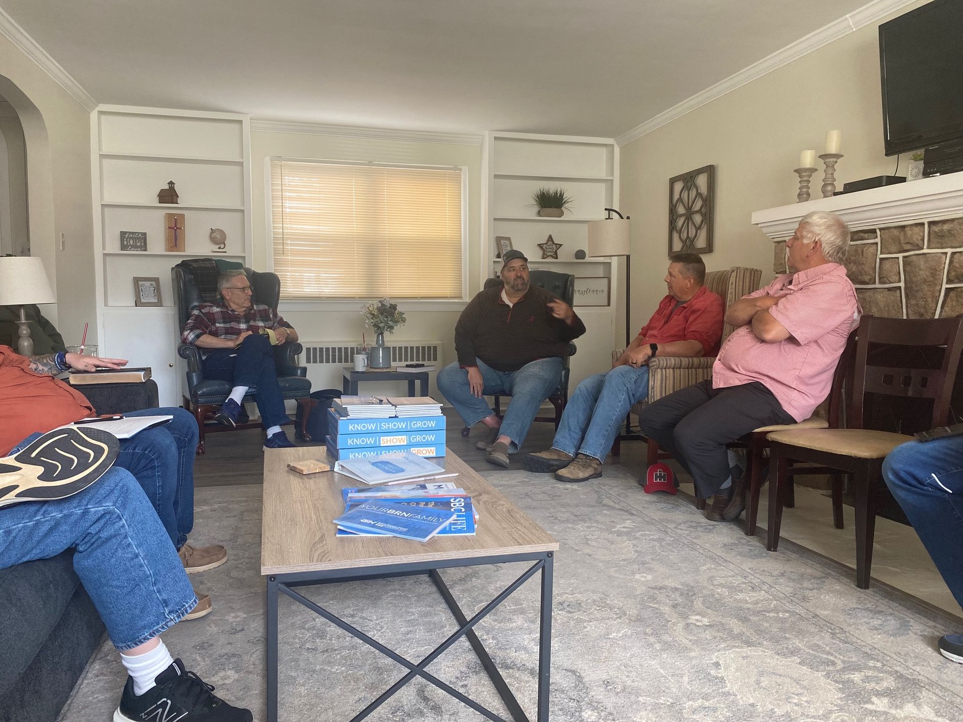 A group of men are sitting around a table in a living room.