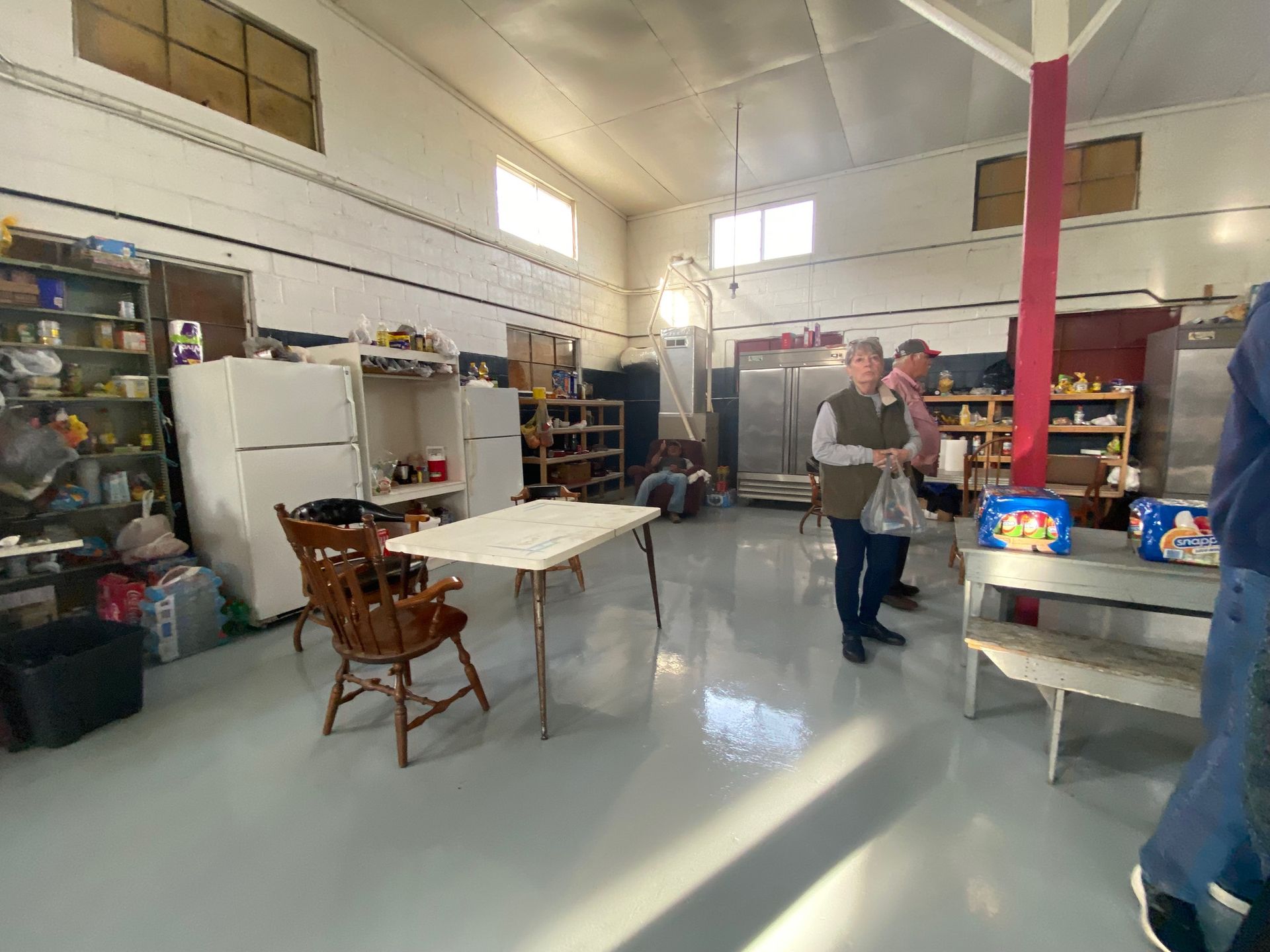 A group of people are standing in a large room with tables and chairs.