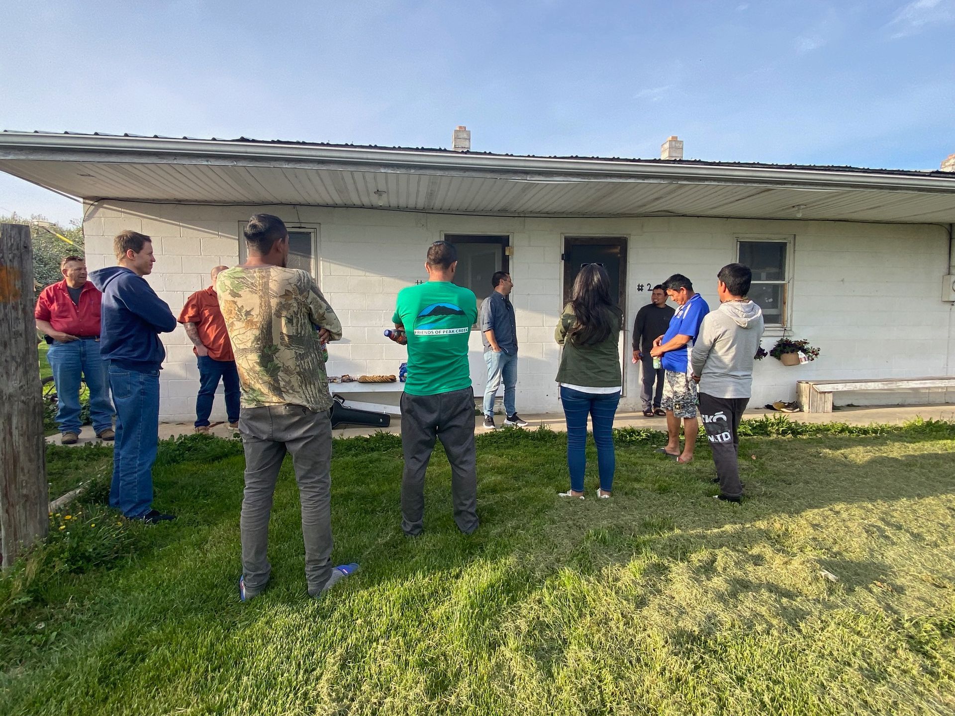 A group of people are standing in front of a white house.
