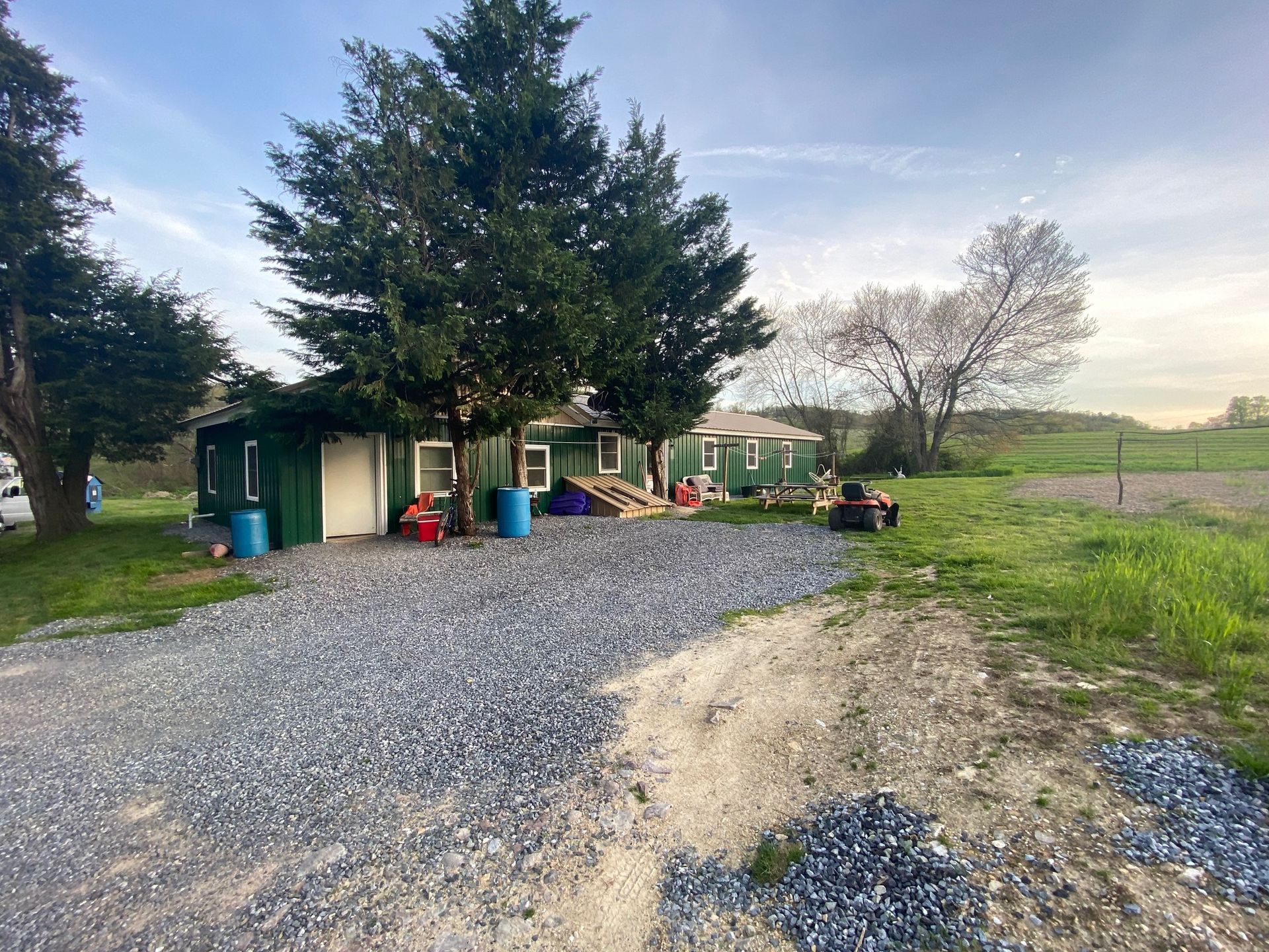 A house is sitting in the middle of a field next to a gravel road.