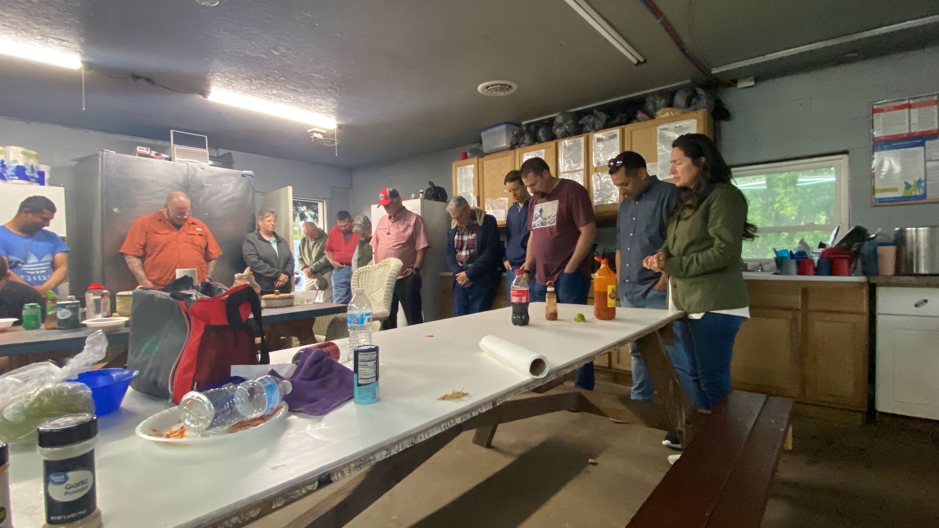 A group of people are standing around a picnic table in a room.