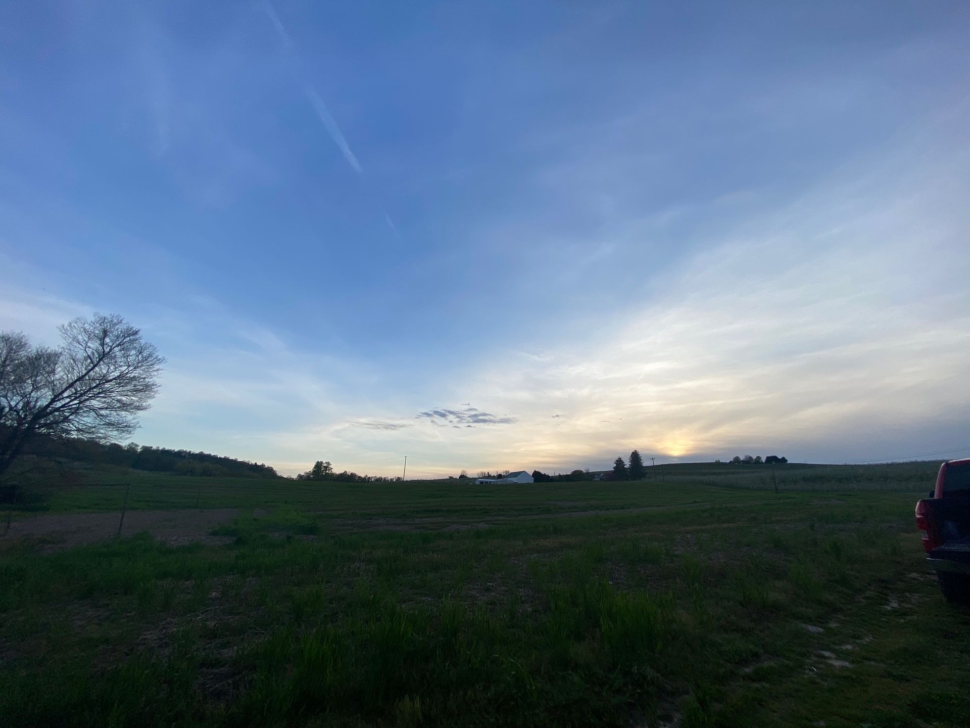 A sunset over a grassy field with a car parked in the foreground.