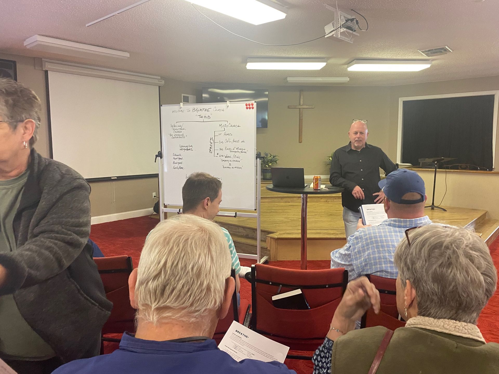 A group of people are sitting in a room with a man standing in front of them