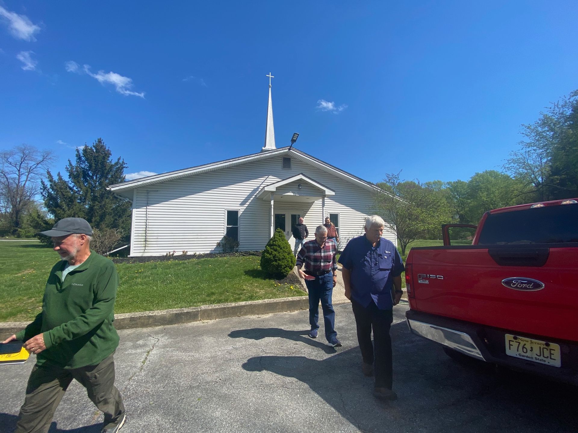 A group of men are standing in front of a church next to a red truck.