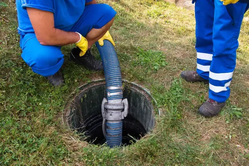 A man is pumping water into a septic tank with a hose.