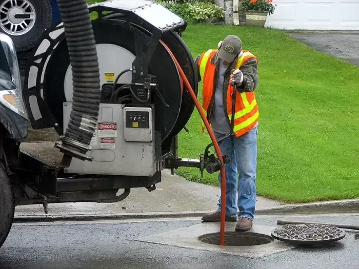 A man is working on a manhole cover with a vacuum cleaner.