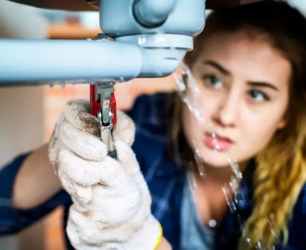 A woman is fixing a leaking pipe with a wrench.