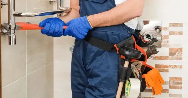 A plumber is fixing a pipe with a wrench in a bathroom.
